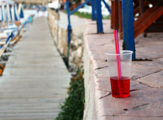Cold red drink with straw at the beach - obrazy, fototapety, plakaty
