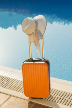 Orange suitcase and white hat next to the swimming pool