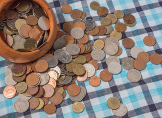 Pile of coins Baht currency is poured out the Pottery cup on the loincloth silk background.
