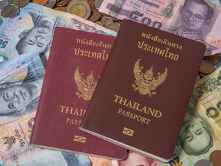 Passport of Thailand on the pile of coins and Banknotes baht currency.