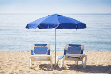 Two sun beds with blue umbrella on a tropical beach with a beautiful ocean view in focus