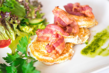 fried eggs with bacon and green salad on the white plate