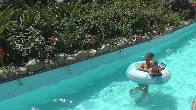 Two women and baby smile and floating on swimming circles  on a slow river in tropical garden
