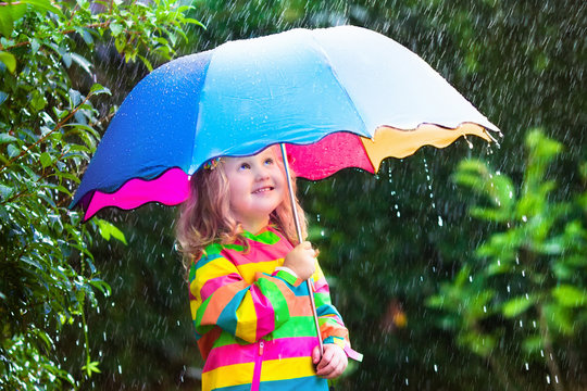 Little girl playing in the rain under umbrella