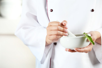 Cook hands with mortar with herbs on bright background