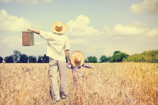 Man and boy wearing straw hats with valize in the farm field
