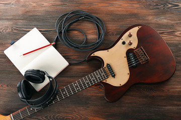 Naklejka premium Electric guitar with headphones and notebook on wooden table close up