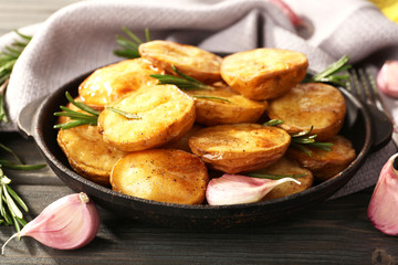 Delicious baked potato with rosemary in frying pan on table close up