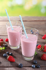 Glasses of berry smoothie on wooden table on blurred background