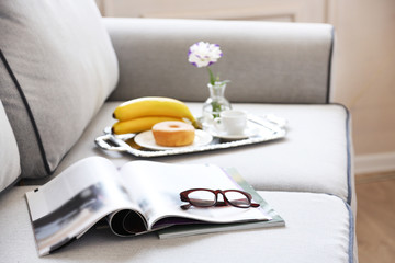 Light breakfast and magazines on sofa in living room, close up