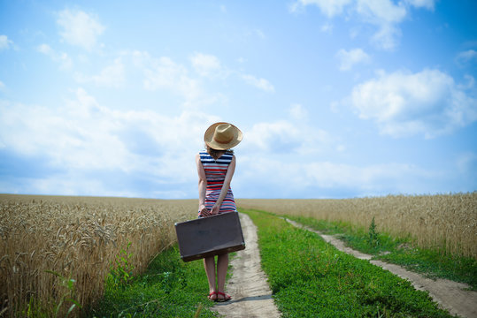 Backview of woman with suitcase on road in wheat field