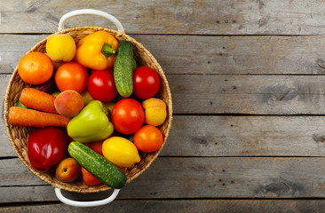 Heap of fresh fruits and vegetables in basket on wooden table close up