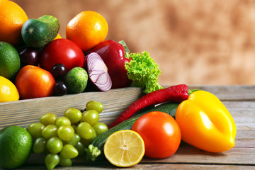 Heap of fresh fruits and vegetables in crate on wooden table close up