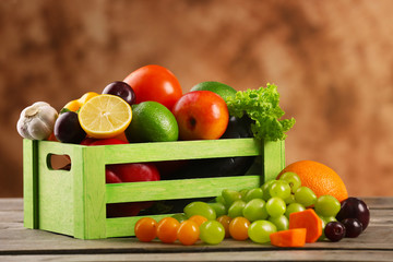Heap of fresh fruits and vegetables in crate on wooden table close up