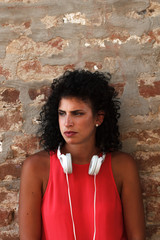 Portrait of young woman with headphones against brick wall. Looking serious 