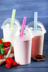 Plastic cups of milkshake on color wooden background