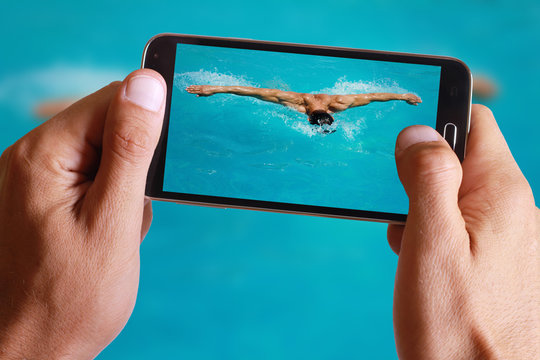 Male hand taking photo of Strong athletic man swimming butterfly style in the pool with cell, mobile phone.