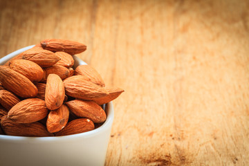 Almonds in bowl on wooden background