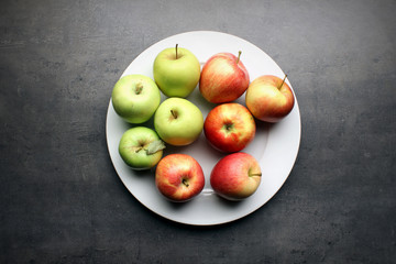 Fresh apples on big white plate and grey kitchen table background
