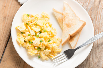 Scrambled egg and bread on white plate. Top view.