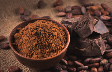 Raw cocoa beans, clay bowl  with cocoa powder, chocolate on sack