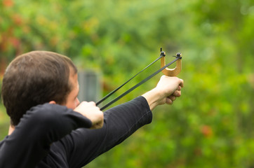 Handsome man concentrated aiming  a slingshot at park having fun
