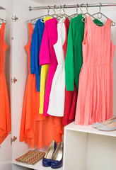 row of bright colorful dress hanging on coat hanger, shoes and h