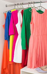 row of bright colorful dress hanging on coat hanger, shoes and h