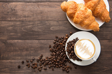 Coffee cup and fresh baked croissants on wooden background. Top