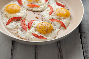 Hot pan with fried eggs and small pieces of tomato