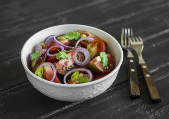 fresh salad with tomatoes in a white bowl on a dark wooden surface