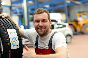 Mechaniker zeigt auf Energielabel eines neuen Autoreifens - Reifenwechsel KFZ // energy label of a...