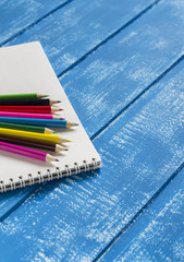 Colored pencils and notebook on a  wooden surface