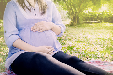 Young pregnant woman relaxing in park outdoors,