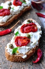 toast of rye bread with different seeds with ricotta cheese, sun-dried tomatoes, capers, parsley and olive oil.