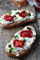 toast of rye bread with different seeds with ricotta cheese, sun-dried tomatoes, capers, parsley and olive oil.