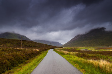 Road in the fields, dark cloudy sky. Isle of Skye, Scotland