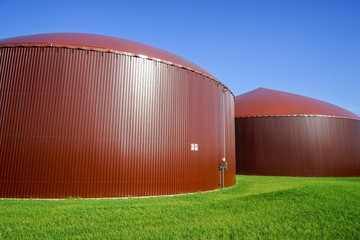 Zwei braune Gärbehälter einer Biogasanlage stehen im grünen Gras