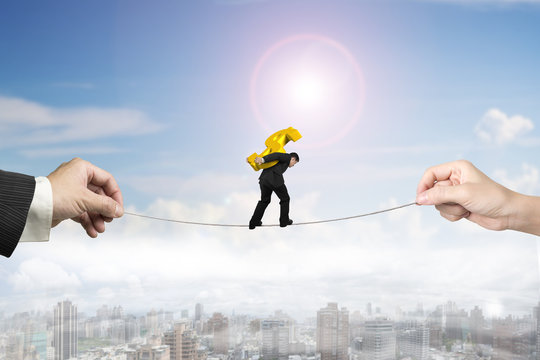 Businessman carrying dollar sign balancing tightrope with hands