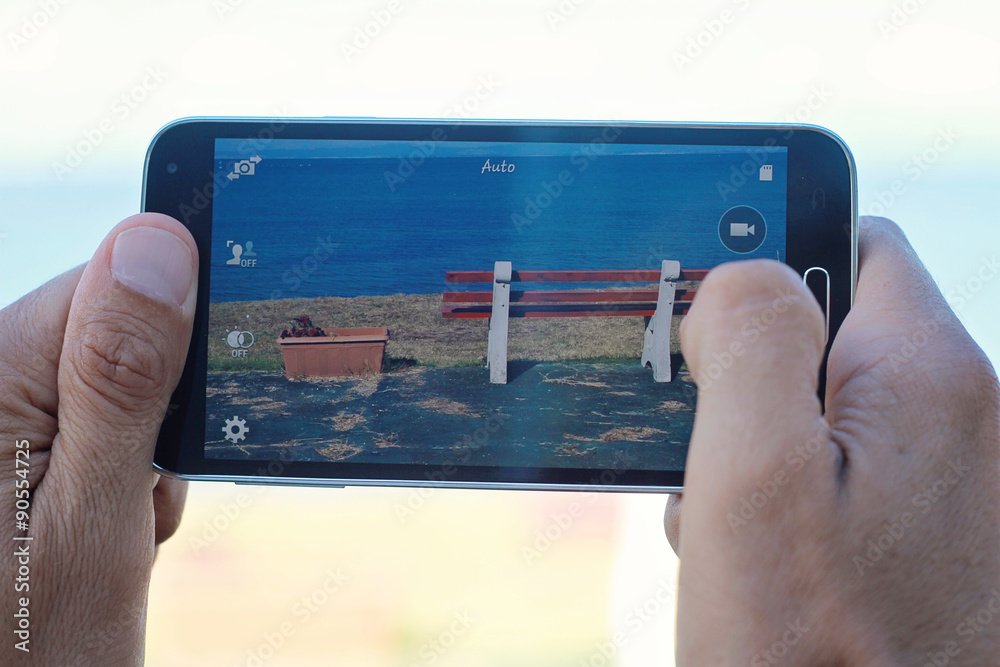 Wall mural close up on male hands taking photo of sea coast with mobile cell phone. summer beach holiday vacati