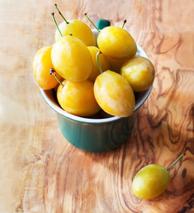 Yellow plum in a green cup on wooden texture