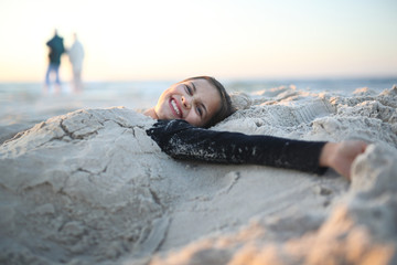 Plaża,radość i zabawa.
Roześmiana, szczęśliwa dziewczynka leży na piaszczystej plaży - obrazy, fototapety, plakaty