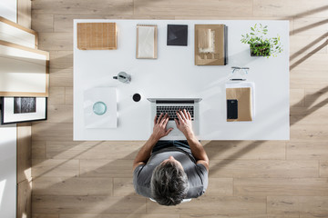top view, a man sitting at tidy desk and working on his laptop