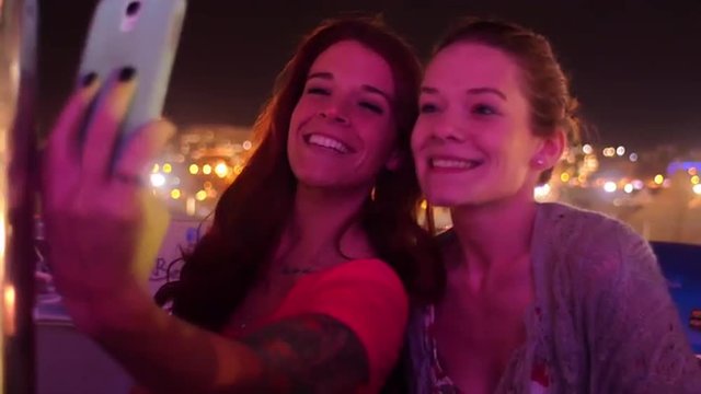 Two friends take selfies on a ferris wheel at night
