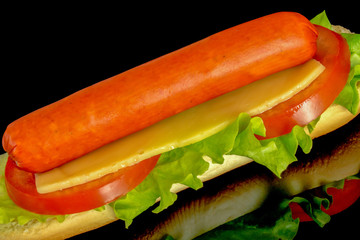 hot dog with fresh leaf lettuce two slices of tomato with reflection isolated on black background

