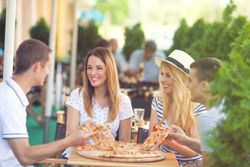 Vier vrolijke jonge vrienden die pizza delen op een terras