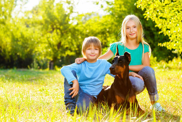 blonde girl and boy hugs beloved dog or doberman in summer park - 90572944