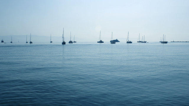 Fototapeta Sailing boats at anchor on a horizon line in a soft blue sea