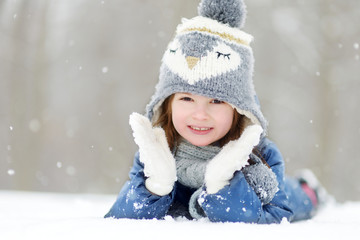 Funny little girl having fun in beautiful winter park during snowfall