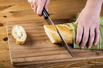 Woman's hands cutting bread on the wooden plank